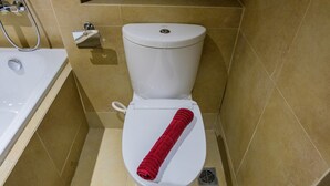 A bathroom with a white toilet, beige tiled walls, and a red towel on the seat.