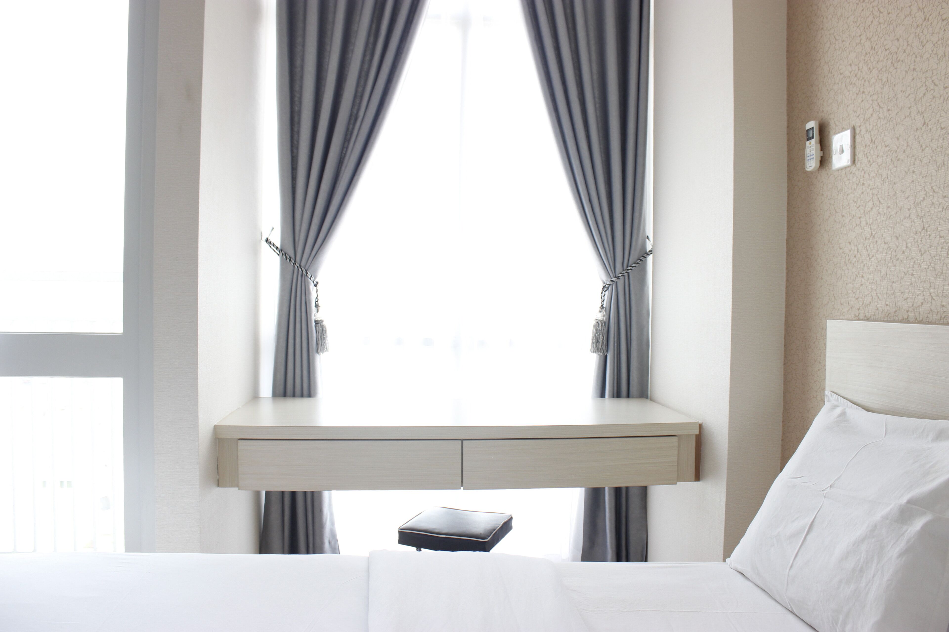 Una habitación de hotel con cama, mesita de noche y ventana con cortinas.