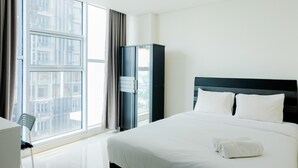 Een hotelkamer met een groot raam, een bed met witte lakens, een donker hoofdeinde en een hoge kast.