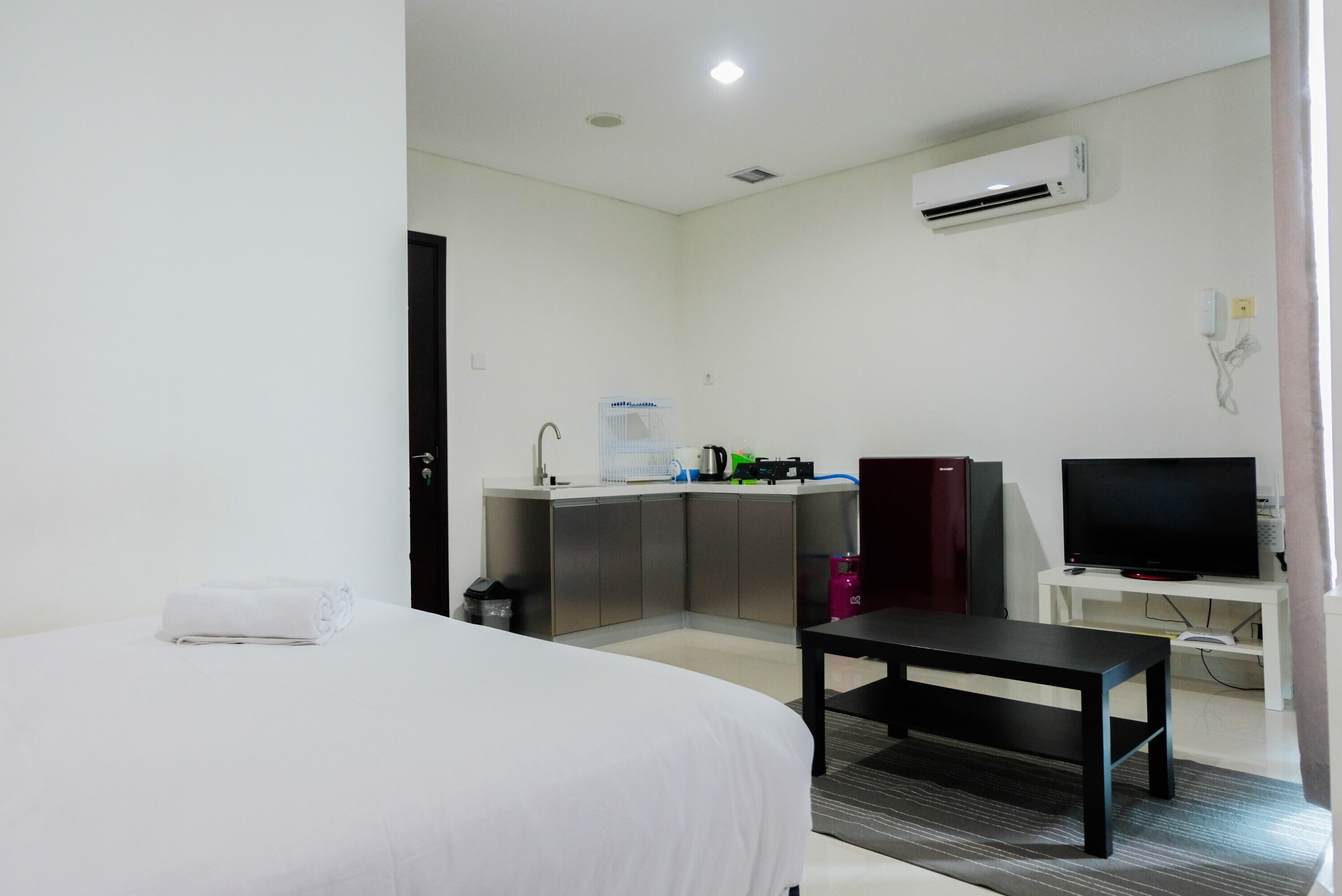 Habitación de hotel con cama, escritorio, televisor, kitchenette y aire acondicionado.
