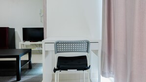 Een wit bureau met een grijze stoel, een televisie op een witte standaard en een zwarte tafel.