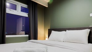 Hotelkamer met een bed, witte lakens, een raam met gordijnen en uitzicht op de stad 's nachts.
