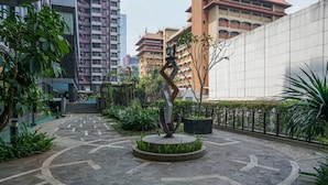 A courtyard with a central sculpture, surrounded by a patterned stone floor and greenery. - Cozy Studio at Tamansari Semanggi Apartment (Jakarta)