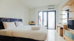 A hotel room with a bed, a TV, and a sliding glass door to the balcony. - Cozy Studio at Tamansari Semanggi Apartment (Jakarta)