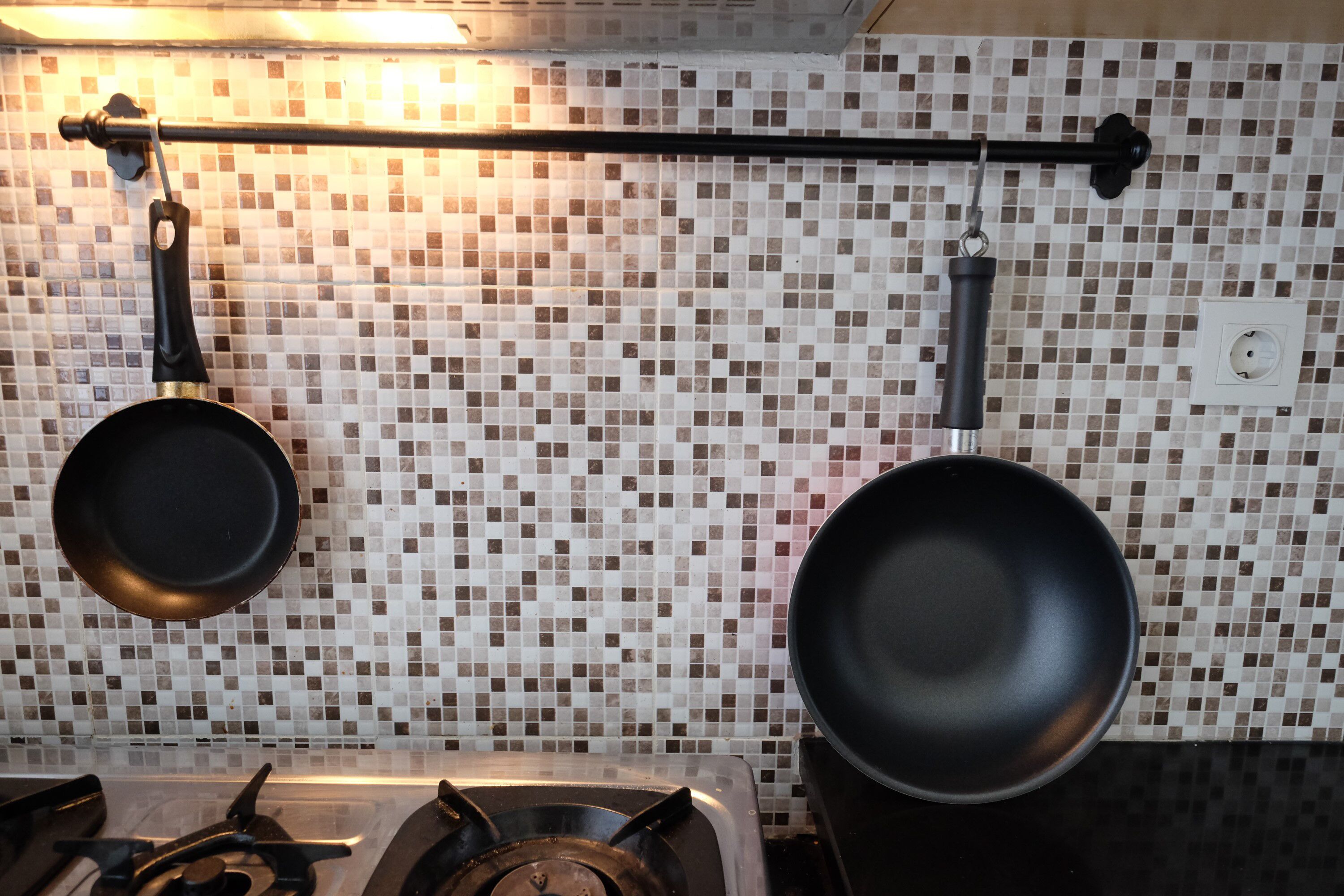 Uma cozinha com painel de azulejos, fogão a gás e duas panelas penduradas.