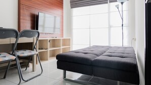 A modern room with a sofa, two chairs, a TV mounted on a wooden wall, a large window with blinds, and a floor lamp. - Elegant 1BR Apartment at Casa De Parco near AEON Mall (Pagedangan)