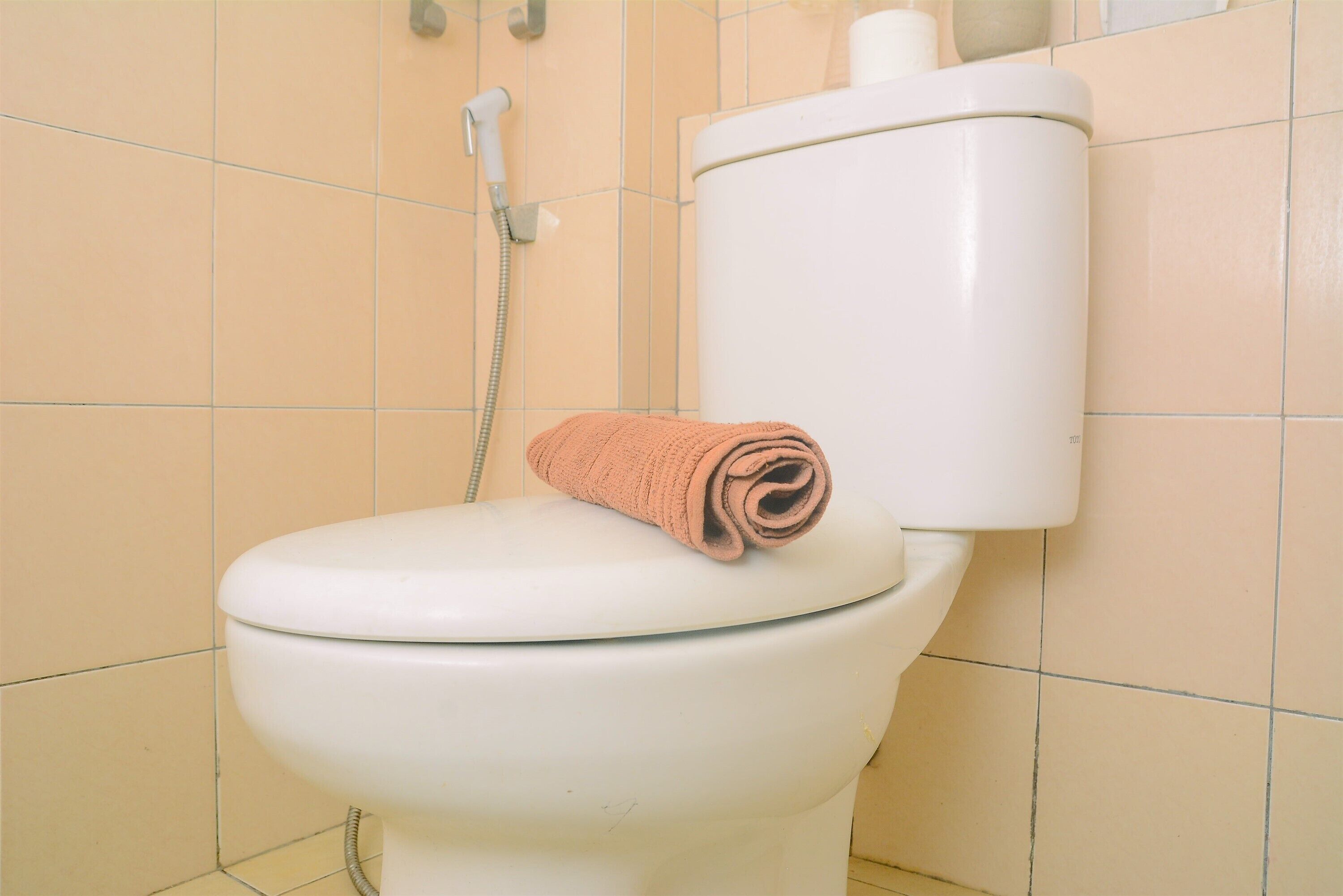 A white toilet with a towel on the lid, a showerhead, and beige tiled walls.