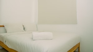 Un letto singolo con biancheria e cuscini bianchi, una testiera in legno e una finestra con persiana.