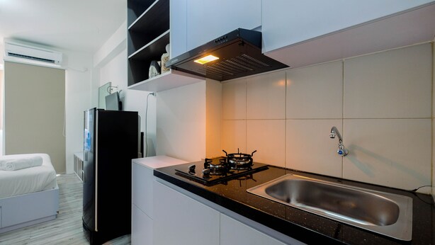 A compact kitchen with a gas stove, a stainless steel sink, and white cabinetry. - Affordable Price Studio at Jababeka Riverview Apartment Cikarang (Cikarang)
