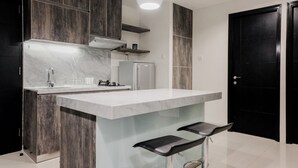 Una cuina moderna amb armaris de fusta fosca, un taulell de marbre blanc, un refrigerador d'acer inoxidable i dos tamborets de bar.