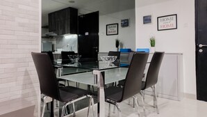 Una zona de menjador moderna amb una taula de vidre, cadires negres i una cuina al fons.