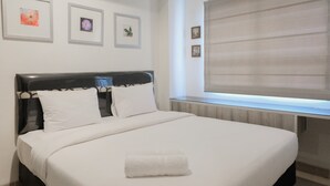 Un llit ben fet amb llençols blancs i una tovallola doblada, amb una capçal i una finestra amb persianes.