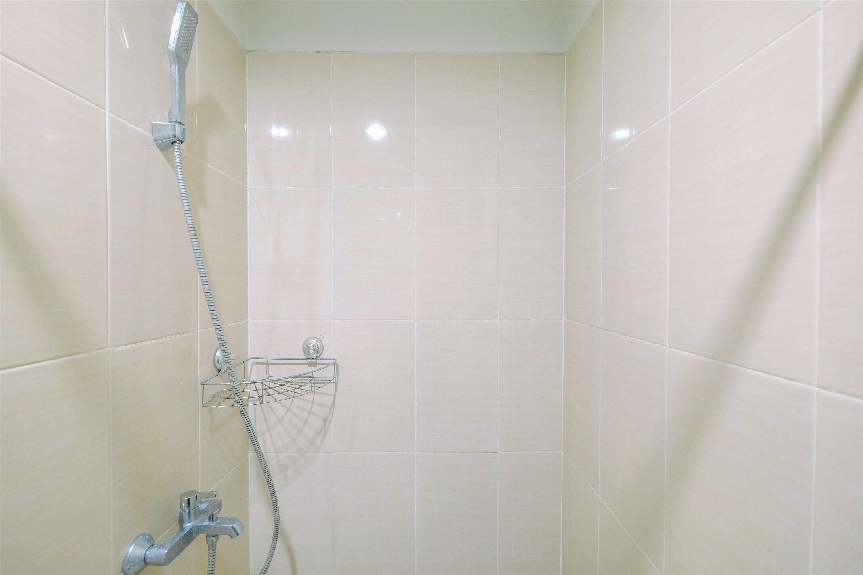 Baño con azulejos blancos, ducha con cabezal de ducha manual y grifo empotrado en la pared, además de un perchero metálico.