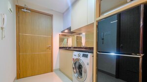 A compact laundry room with a washing machine, a refrigerator, and a wooden door. - Exclusive Studio at The Oasis Cikarang Apartment (Cikarang)