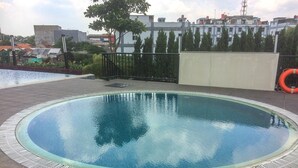 A rooftop swimming pool with a clear blue water surface, surrounded by a tiled deck and a metal railing. - Exclusive Studio at The Oasis Cikarang Apartment (Cikarang)