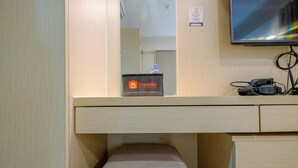 A traveler's room with a bed, a small table with a water bottle, a travel bag, and a TV mounted on the wall. - Exclusive Studio at The Oasis Cikarang Apartment (Cikarang)