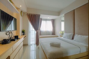 Une chambre d’hôtel moderne dotée d’un grand lit, d’un téléviseur à écran plat fixé au mur, d’un bureau avec un ordinateur et un téléphone, et d’une fenêtre avec des rideaux.