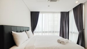 Una habitación de hotel con una cama grande, cortinas oscuras y un cabecero blanco.