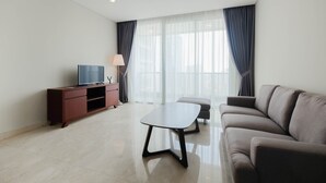 Una sala moderna con un sofá, una mesa de centro, un televisor sobre un mueble de madera y un ventanal con cortinas.
