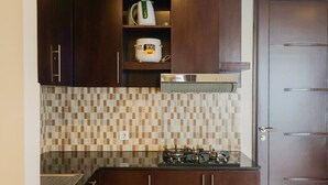 A compact kitchen with dark wooden cabinets, a tiled backsplash, and a gas stove. - Exclusive 2BR @ The Empyreal Condominium Epicentrum Apartment (Jakarta)