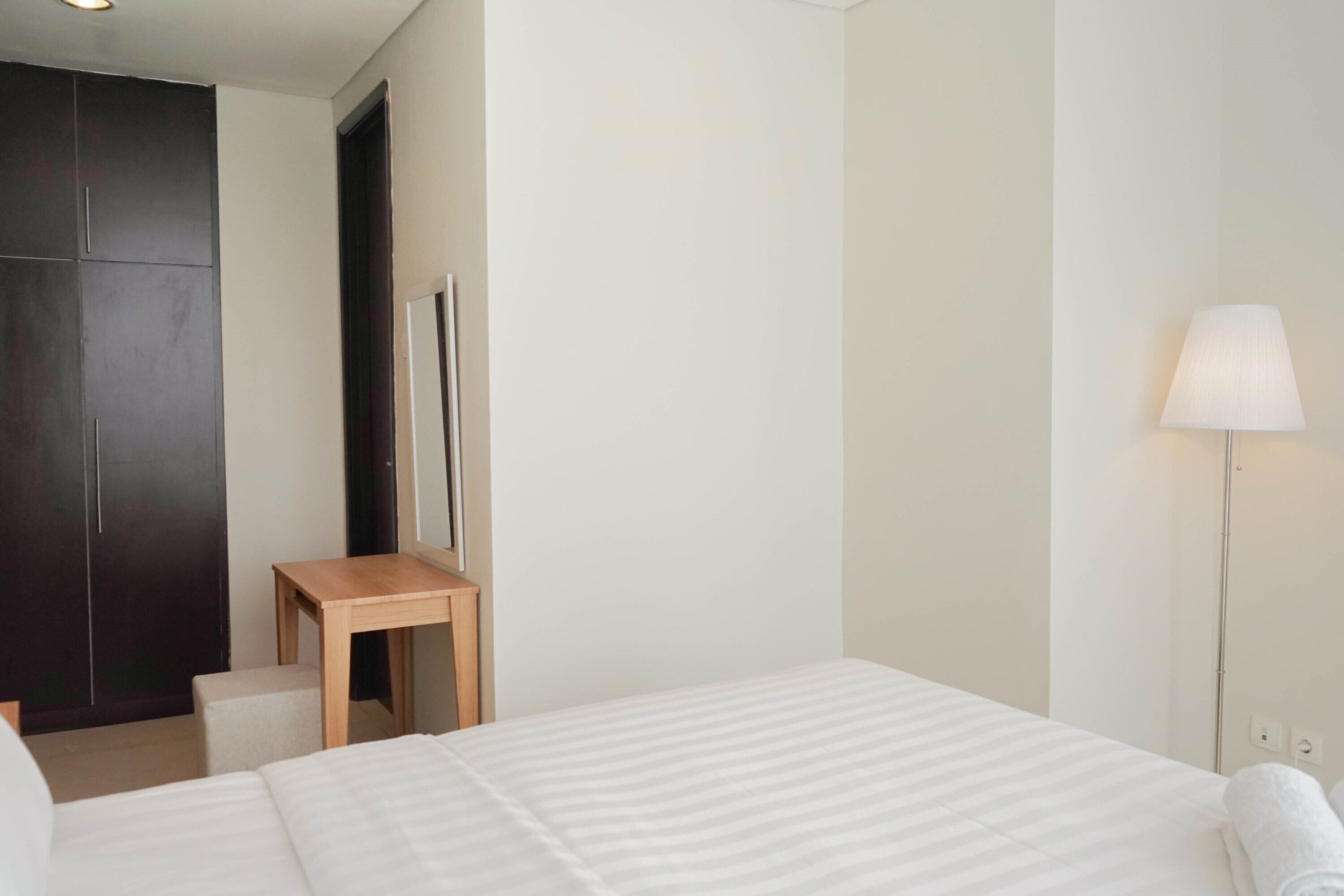 A hotel room with a bed, a desk, a wardrobe, and a lamp.