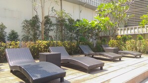Outdoor wicker lounge chairs arranged on a wooden deck with a backdrop of greenery and a building with a balcony. - Exclusive 2BR @ The Empyreal Condominium Epicentrum Apartment (Jakarta)