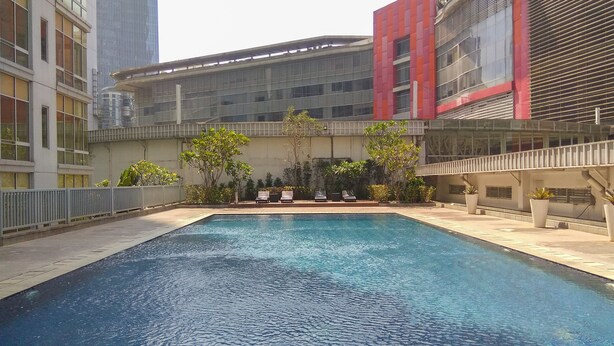 A swimming pool with lounge chairs, surrounded by buildings with large windows and balconies. - Exclusive 2BR @ The Empyreal Condominium Epicentrum Apartment (Jakarta)