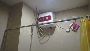 A bathroom with a white water heater mounted on the wall, a showerhead, and a curtain rod with a yellow shower curtain. - Cozy Studio near UNPAD at Taman Melati Apartment Jatinangor (Hegarmanah)