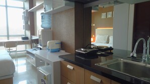 A modern hotel room with a kitchenette, a large water dispenser, a coffee maker, a toaster, and a bed with white bedding. - Cozy Studio near UNPAD at Taman Melati Apartment Jatinangor (Hegarmanah)