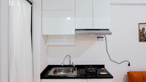A compact kitchen with a stainless steel sink, a gas stove, and white cabinets. - Pleasant 2BR Apartment at Bassura City near Shopping Mall (Jakarta)