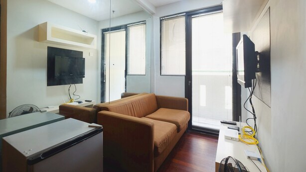 A modern room with a sofa, a desk, a flat-screen TV, and a window with blinds. - Best Choice 1BR Apartment at Kebagusan City (Jakarta)