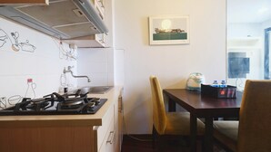 A kitchen with a gas stove, a sink, and a dining area with a table and chairs. There is a framed picture on the wall and a bag on the table. - Best Choice 1BR Apartment at Kebagusan City (Jakarta)