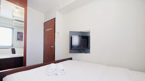 A hotel room with a bed, a TV mounted on the wall, a wooden door, and a mirror reflecting part of the room. - Best Choice 1BR Apartment at Kebagusan City (Jakarta)