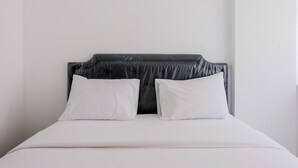 A bed with a dark headboard and white pillows, set against a plain wall. - Comfortable and Fully Furnished Studio at Poris 88 Apartment (Tangerang)