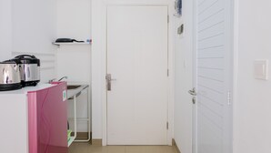 A compact kitchen with a white door, a sink, a small countertop, and a pink refrigerator. - Comfortable and Fully Furnished Studio at Poris 88 Apartment (Tangerang)