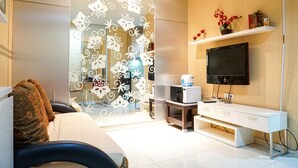 Una sala de estar moderna con un sofá, un televisor montado en la pared, una mesita y un separador decorativo con motivos florales.