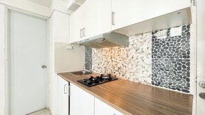 Kompakti keittiö, jossa on valkoiset kaapit, puinen työtaso ja kivikuvioitu välitila.