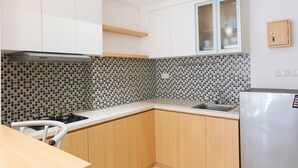 Una cocina compacta con armarios blancos, salpicadero de azulejos, estufa a gas y lavamanos integrado.