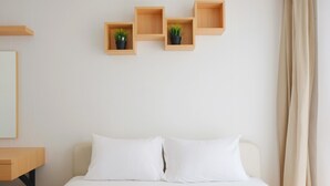 Una habitación de hotel con una cama, una mesita de noche de madera y tres estantes de madera con plantas en macetas.