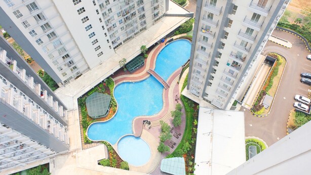 Un edificio de gran altura con piscina en la azotea, varios balcones y un jardín ajardinado.