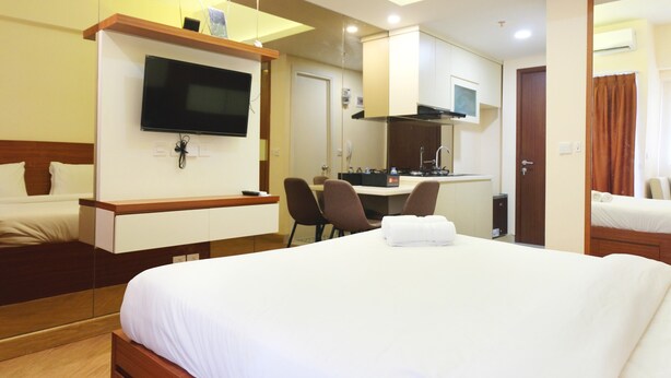 A hotel room with a large bed, a TV mounted on the wall, a desk with chairs, and a kitchenette. - Highest Value Studio Apartment at Parkland Avenue (South Tangerang)