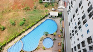 A rooftop swimming pool with three sections, surrounded by greenery and adjacent to a multi-story building. - Highest Value Studio Apartment at Parkland Avenue (South Tangerang)