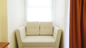 A corner room with a beige sofa and a window with blinds. - Highest Value Studio Apartment at Parkland Avenue (South Tangerang)