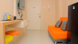 Pieni, kirkkaanväreinen huone, jossa on sohva, seinälle asennettu televisio, työpöytä jakkaroineen ja ovi.