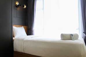 A hotel room with a neatly made bed, a bedside telephone, and a wall-mounted light fixture. - Warm and Cozy 3BR Apartment at M-Town Residence (Gading Serpong)