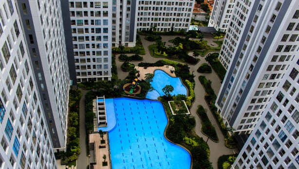 A high-rise hotel with a large swimming pool surrounded by greenery and a children's play area. - Warm and Cozy 3BR Apartment at M-Town Residence (Gading Serpong)