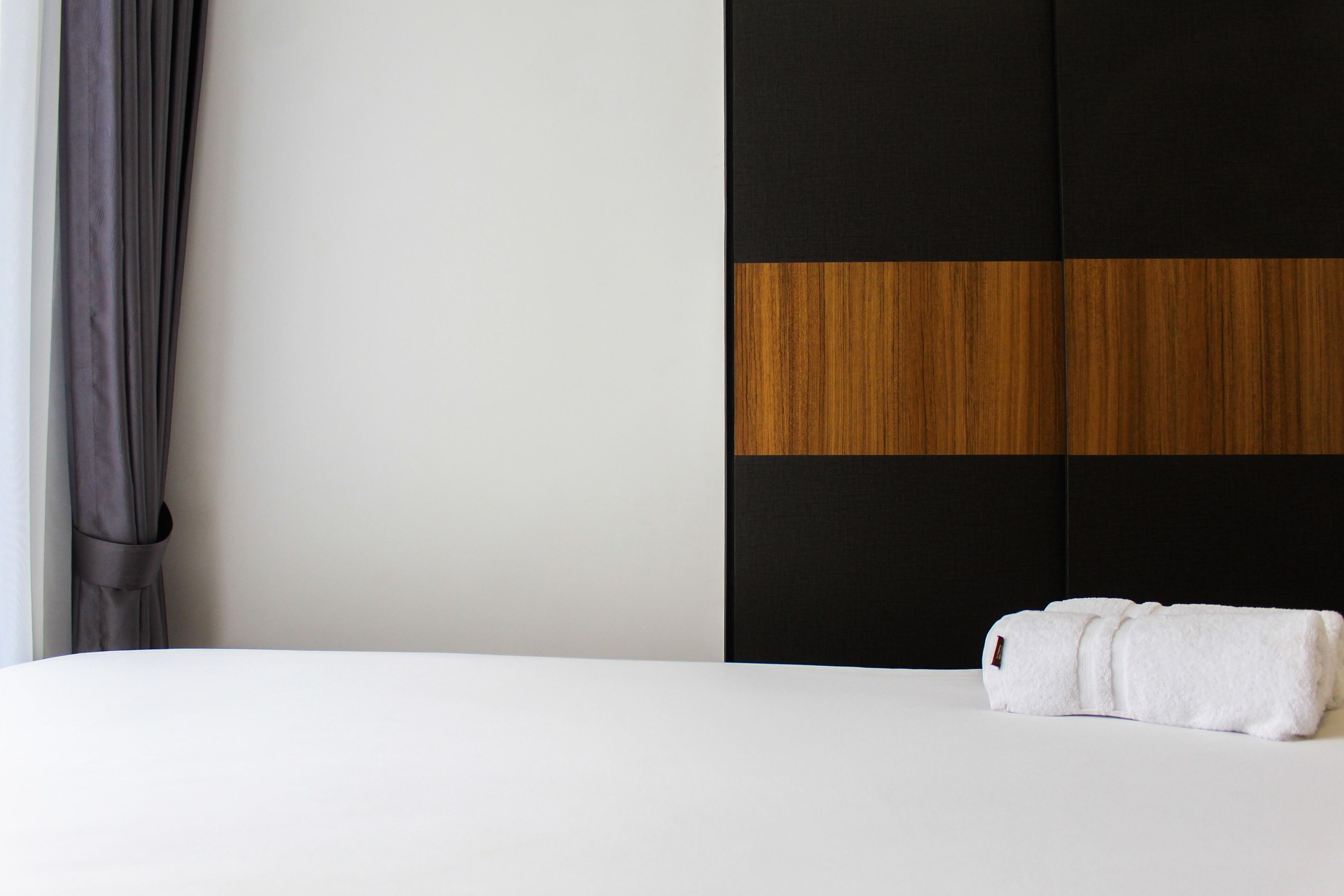 A hotel room with a bed, a grey curtain, and a wardrobe with a black and wooden panel design.