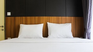 A bed with white bedding and two pillows, a wooden headboard, and a black panel above. - Warm and Cozy 3BR Apartment at M-Town Residence (Gading Serpong)
