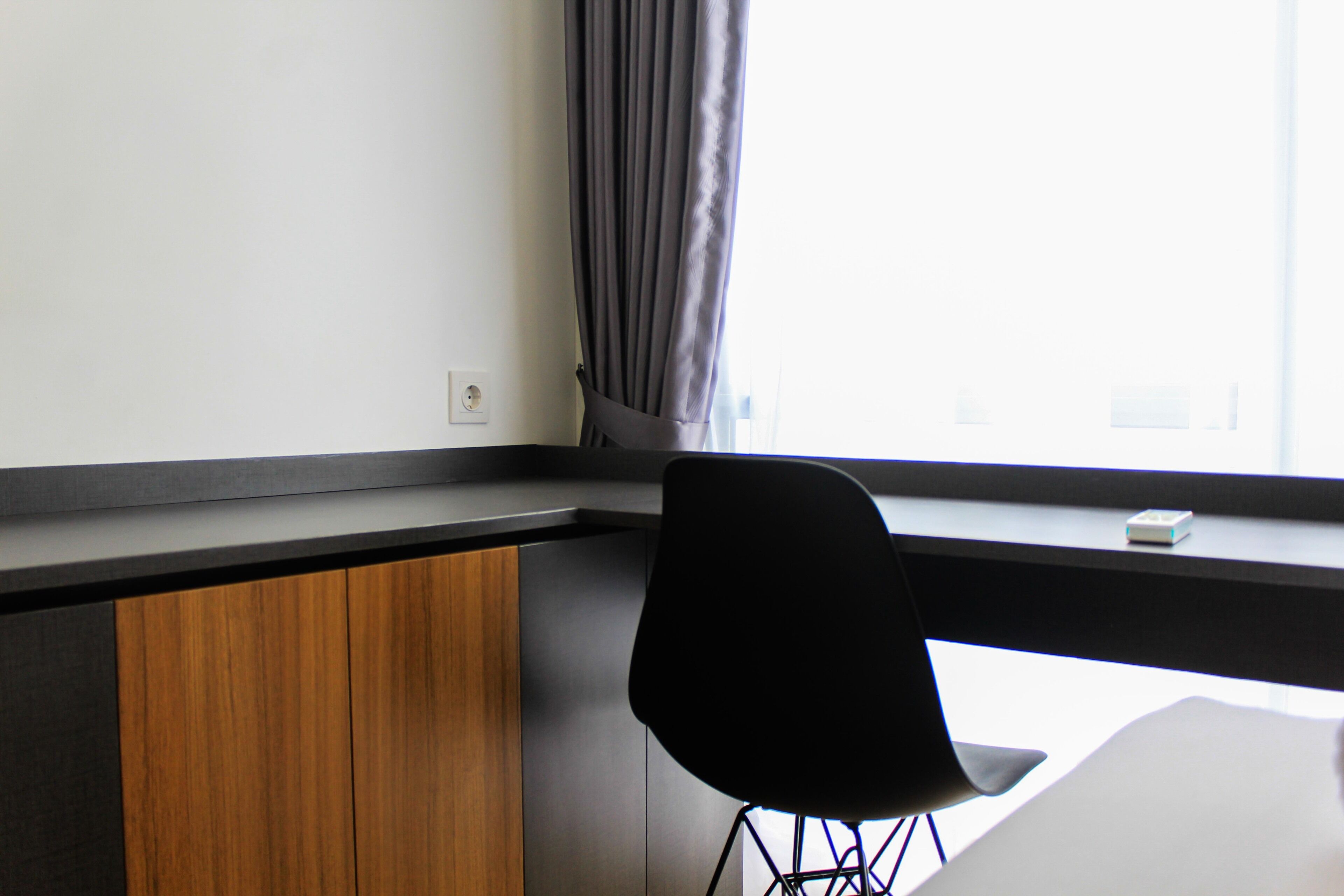 A modern room with a wooden cabinet, a black chair, and a window with curtains.
