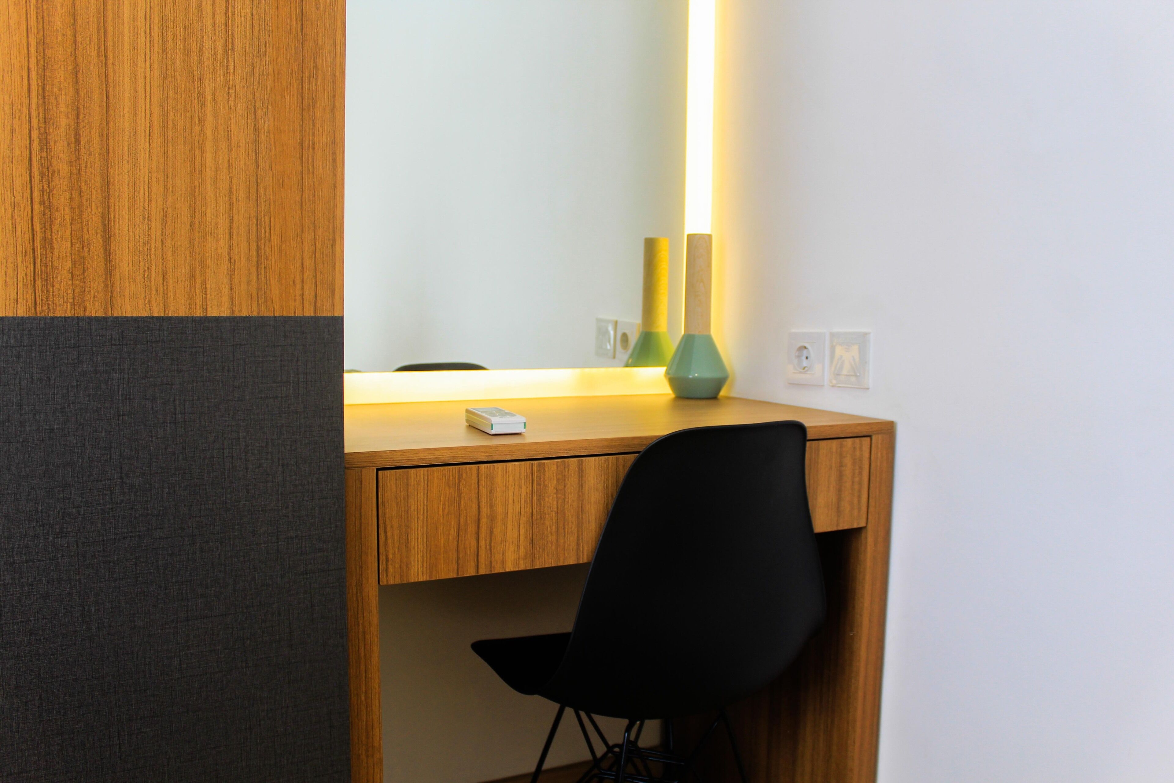A wooden desk with a black chair, a mirror, and two green vases.
